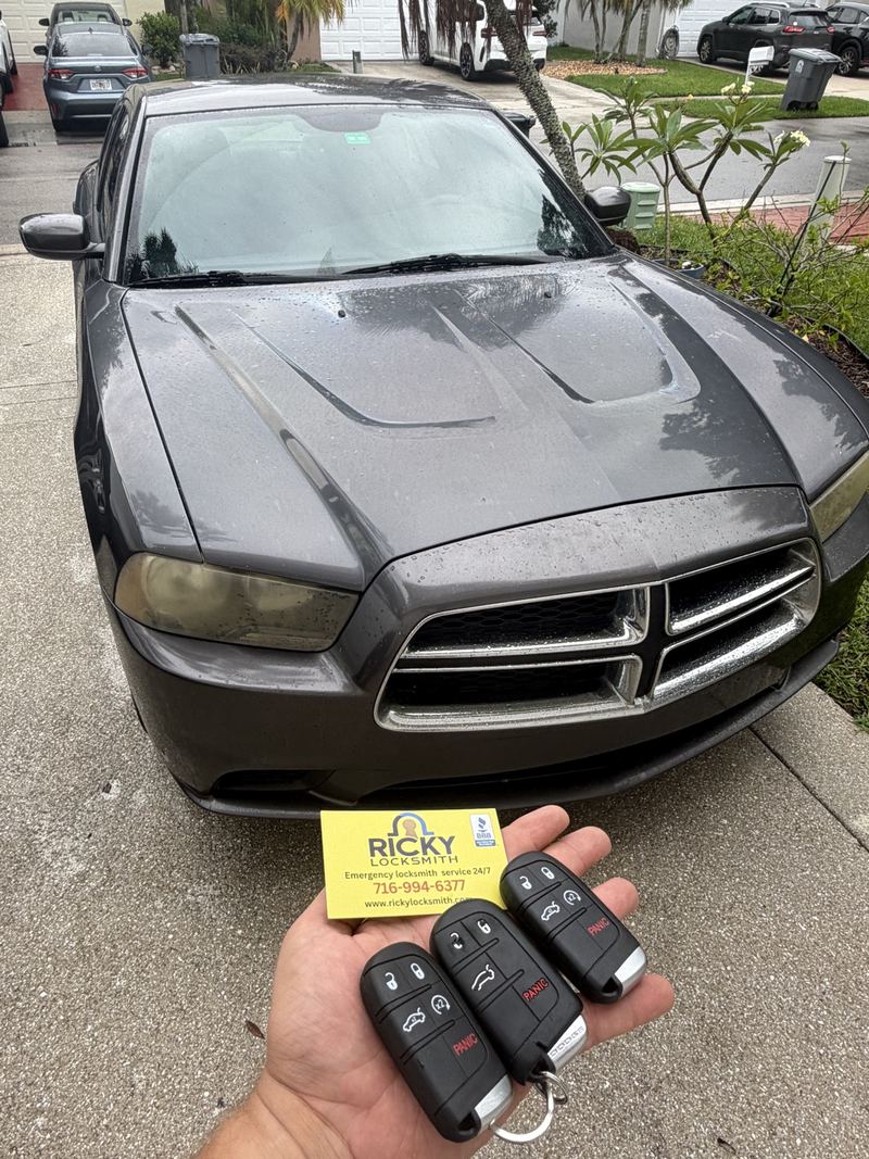 Three Dodge key fobs held in front of a Dodge sedan