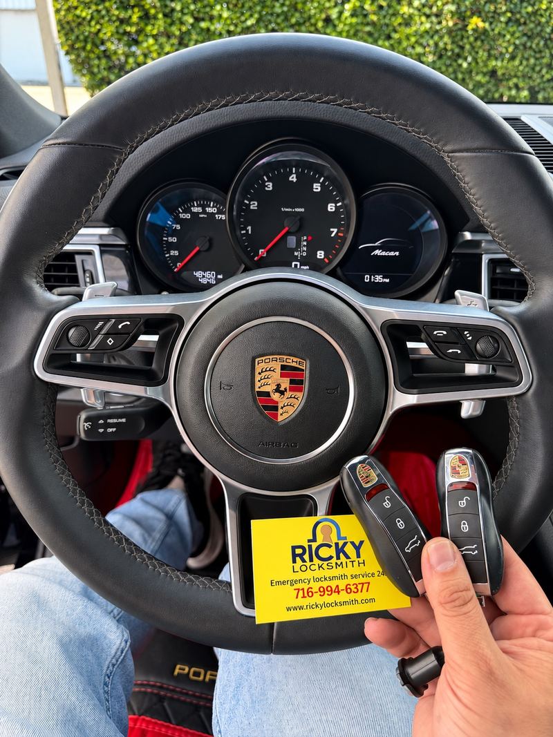 Two Porsche keys and a Ricky Locksmith card beside a Porsche steering wheel